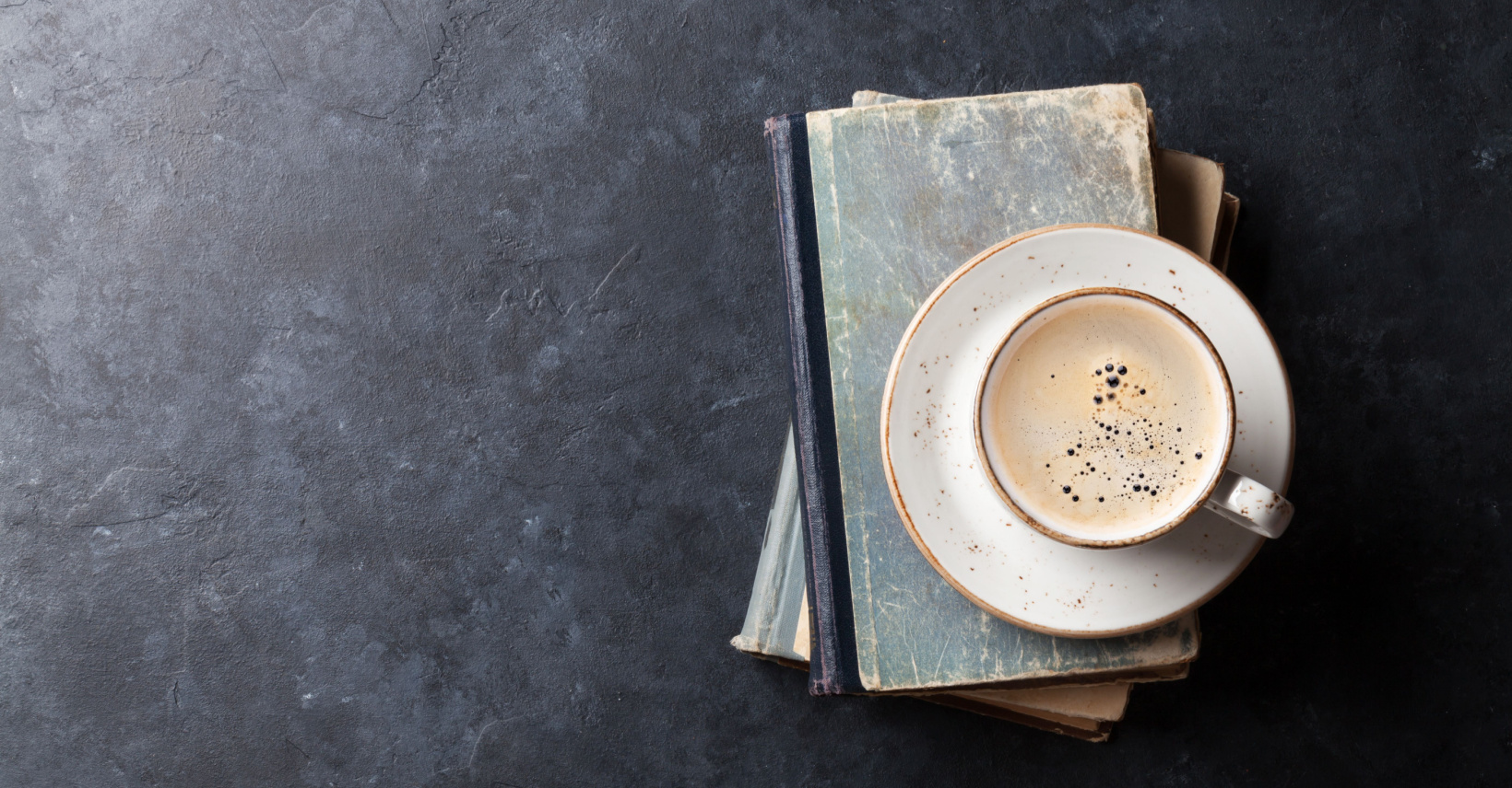 Pile of books with a cup of coffee on the top.